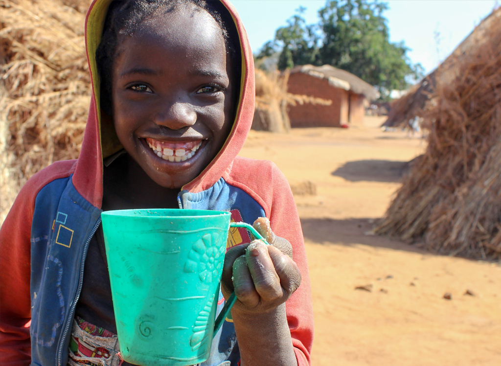 Zambian girl smiling to the camera while drinking a cup of water