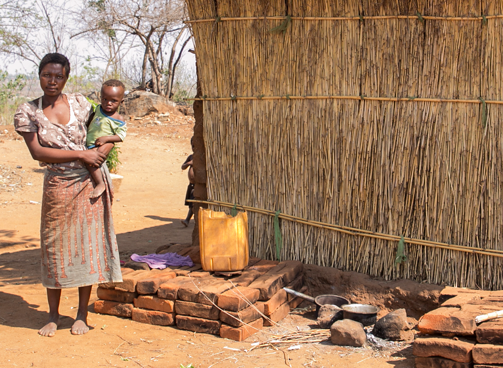 Woman carrying her baby, posing in front of her home