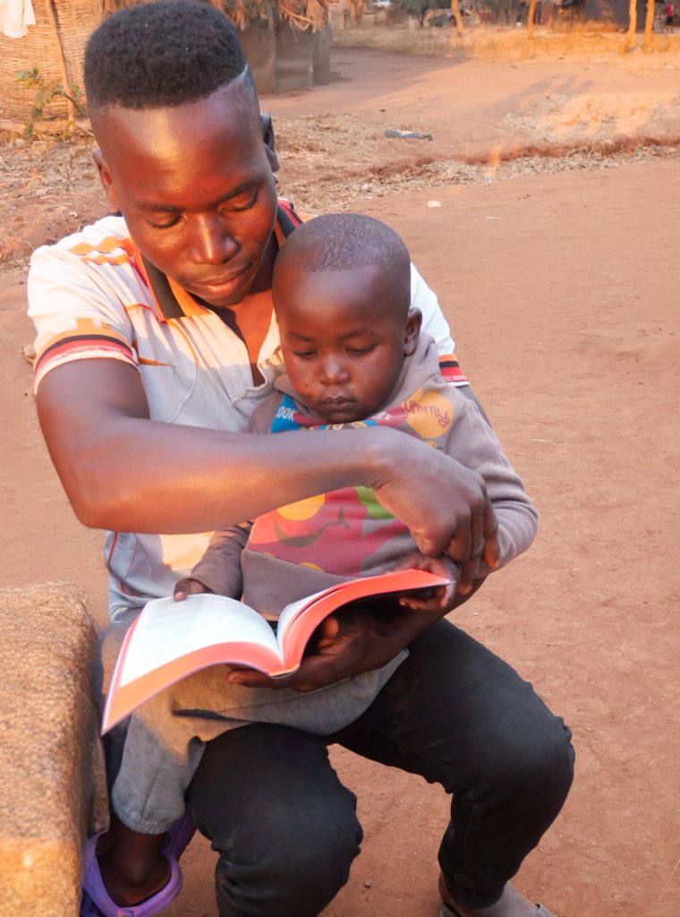 Zambian man sitting with his son on his lap, reading the bible