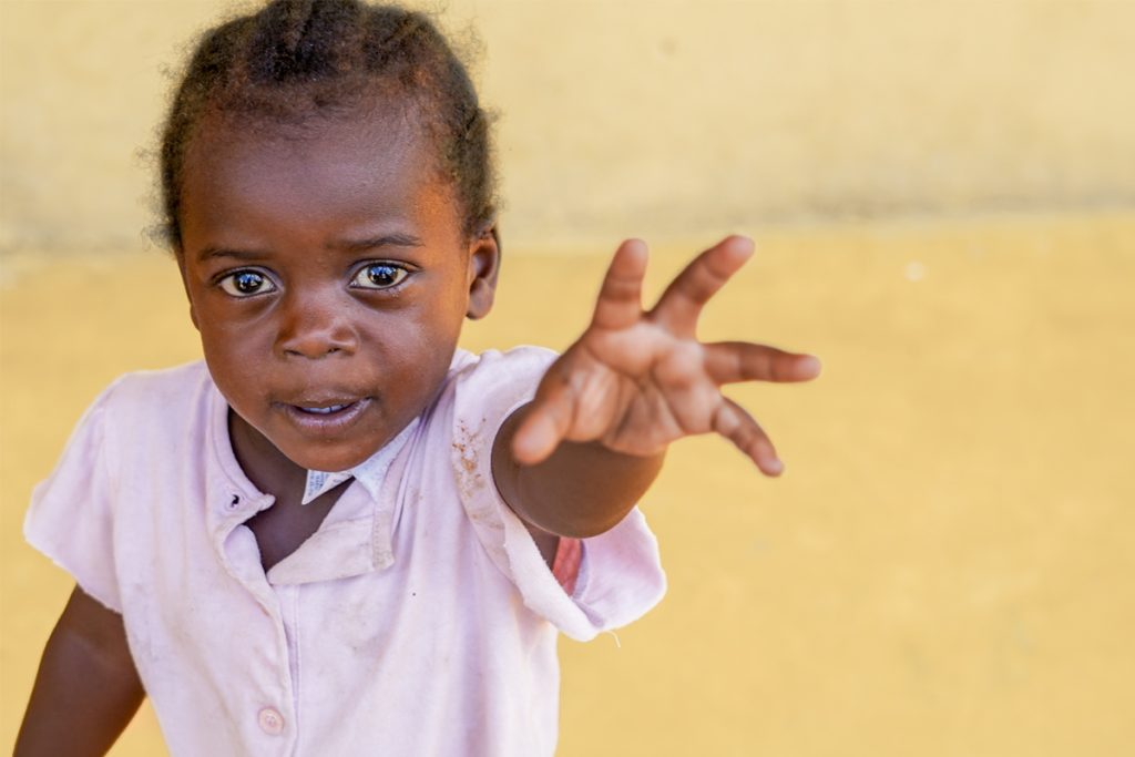 Young girl from a Haitian migrant community in the Dominican Republic reaching out her hand towards the camera.