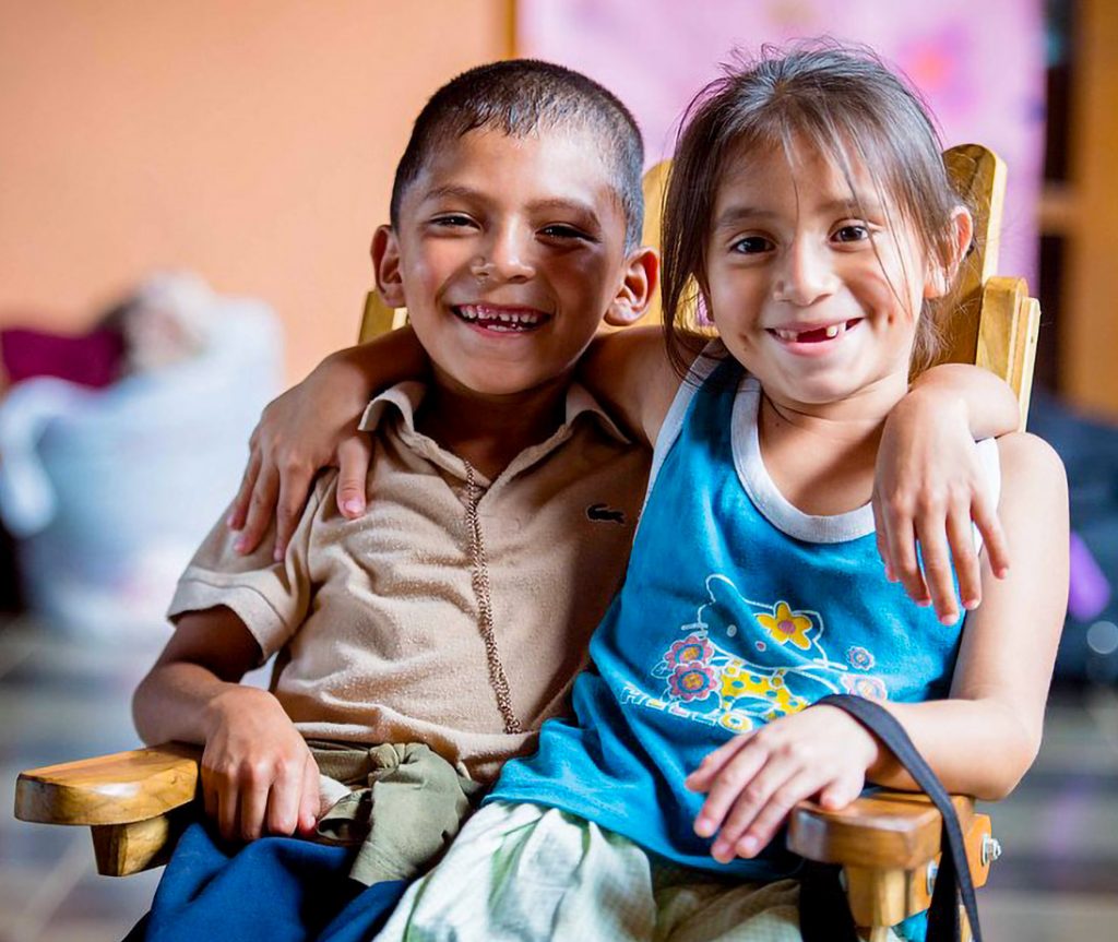 Two Nicaraguan children sitting together, arms over each other's shoulders, smiling for the camera.